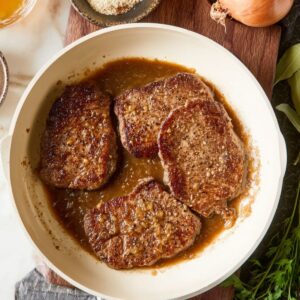 Healthy Smothered Cube Steak Recipe 16 Golden-brown cube steaks cooked and ready to be smothered with a rich onion and gravy sauce in the pan, alongside seasonings for added flavor