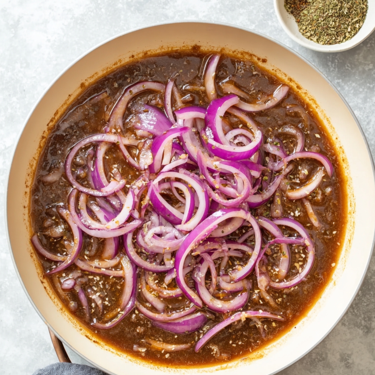 Healthy Smothered Cube Steak Recipe 12 A skillet with sliced red onions and a rich sauce simmering together, preparing the flavorful gravy for smothered cube steak.