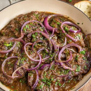 Healthy Smothered Cube Steak Recipe 18 A delicious dish of smothered cube steak in a savory gravy with sliced red onions, garnished with fresh herbs like parsley, and served with slices of bread on the side.