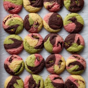 A close-up of a tray of spumoni cookies, showing the marbled dough with contrasting colors of pistachio, cherry, and chocolate, rolled in sugar and arranged neatly on parchment paper.