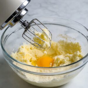 Healthy Strawberry Muffins Recipe 15 A hand mixer beats together butter and sugar in a glass mixing bowl, preparing the base for strawberry muffins. The mixture is light and creamy, and an egg is ready to be incorporated into the batter.