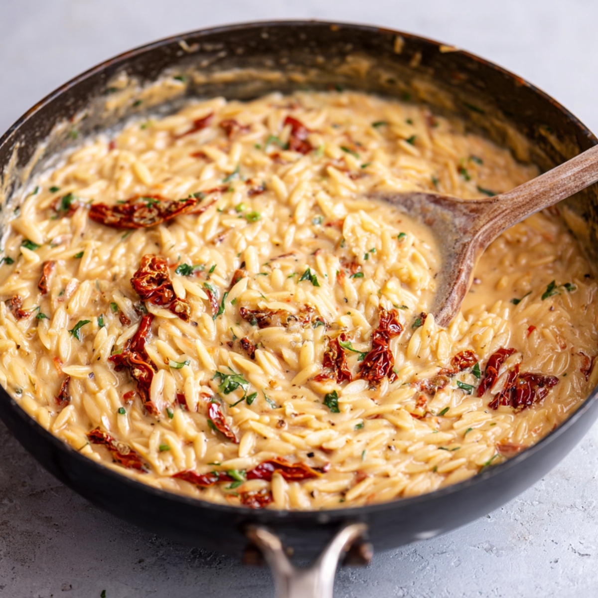 Healthy Tuscan Chicken Orzo Recipe 12 A close-up of a skillet filled with creamy orzo pasta, sun-dried tomatoes, and a smooth, velvety sauce. The orzo is cooked and mixed with herbs and spices, creating a comforting texture and flavor