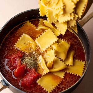 Delicious Vegan Lasagna Soup Recipe 17 Lasagna noodles being added to a bubbling vegan lasagna soup, with tomatoes and seasoning.