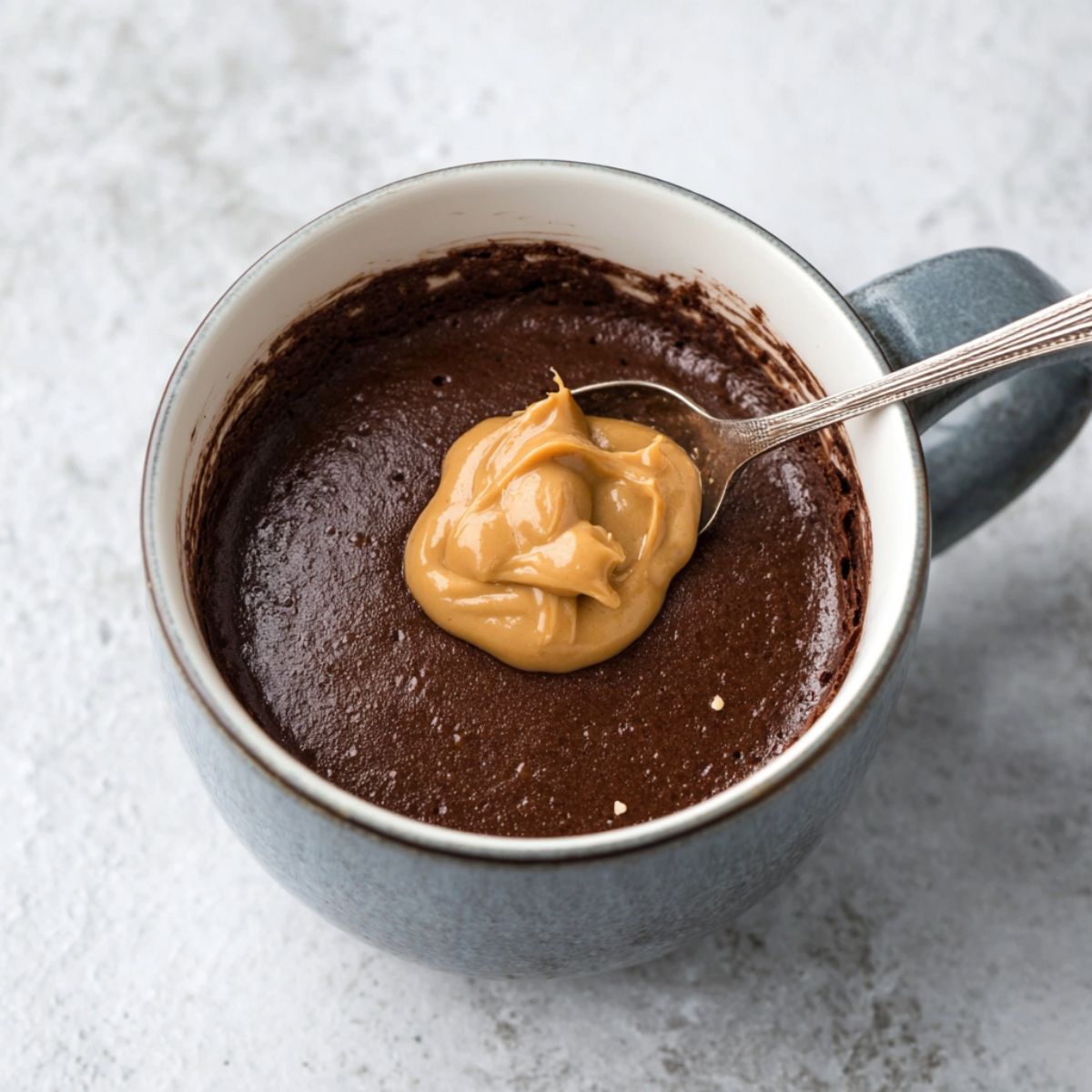 The Best Chocolate Mug Cake Recipe 12 A cup of chocolate cake batter with a dollop of peanut butter on top, ready to be microwaved for a quick dessert.