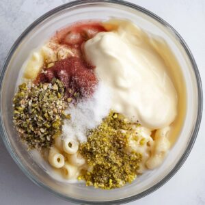 Dressing ingredients for macaroni salad including mayonnaise, mustard, pickles, and seasonings, all combined in a bowl to create a flavorful base for the salad.