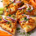 buffalo chicken flatbreads Close-up of baked buffalo chicken flatbread slices garnished with red onion and green herbs, served with celery and carrot sticks.