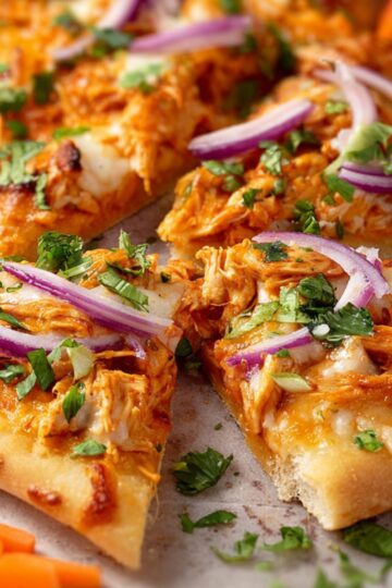 Best Buffalo Chicken Flatbreads Recipe 2 buffalo chicken flatbreads Close-up of baked buffalo chicken flatbread slices garnished with red onion and green herbs, served with celery and carrot sticks.