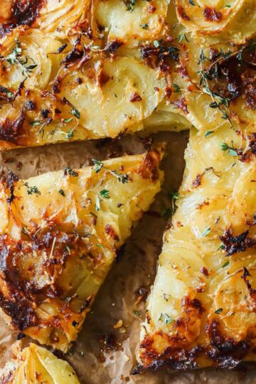 The Best Potato Galette Recipe 3 potato galette Overhead shot of a rustic, golden-brown potato galette with thin potato slices, baked cheese, and herbs, partially sliced with a spatula.