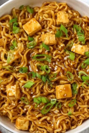 Best Saucy Ramen Noodles Recipe 2 Bowl of saucy ramen noodles garnished with green onions and tofu cubes, ready to eat, with chopsticks on the side.