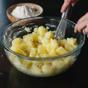 "Mashed potatoes being mixed in a glass bowl with a whisk, preparing for potato cheese pancakes.