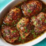 Balsamic Chicken Thighs A white oval baking dish with baked balsamic chicken thighs, richly glazed and garnished with fresh parsley, golden-brown skin, juicy meat, ready to serve, close-up, overhead angle.