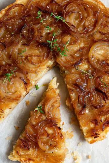 The Best Caramelized Onion Tart Recipe 1 Caramelized Onion Tart Finished baked caramelized onion tart, golden crust, onions glossy and browned, one slice cut, styled on parchment paper with a vintage knife, minimal props.