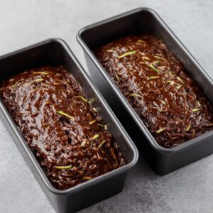 Best Chocolate Zucchini Bread Recipe 16 Two loaf pans filled with unbaked chocolate zucchini bread batter, ready for the oven. The batter is dark brown with visible shreds of zucchini.