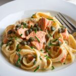 Creamy Salmon Pasta Creamy pasta with salmon pieces and capers, garnished with chopped chives, served on a white plate with the pasta pan in the background.