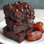 Date Brownies Stack of fudgy chocolate brownies topped with melted chocolate chips on a white plate with dates on the side.