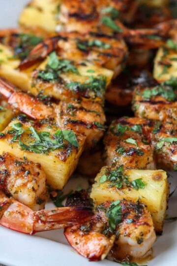 Easy Grilled Pineapple Shrimp Skewers 2 Grilled Pineapple Shrimp Skewers Close-up of grilled shrimp and pineapple skewers on a white plate, garnished with chopped herbs.