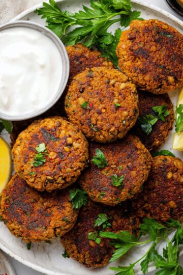Delicious Lentil Patties Recipe 3 Lentil Patties A plate of cooked lentil patties served with lemon wedges, fresh parsley, and small bowls of yogurt sauce and chili oil on the side.