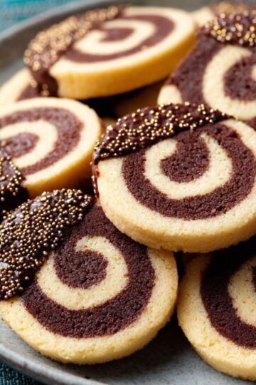 The Best Pinwheel Cookies Recipe 2 Pinwheel Cookies Finished baked pinwheel cookies, some half-dipped in chocolate with gold sprinkles, arranged on a plate.