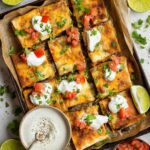 Sheet Pan Crunchwrap A stacked plate of crispy quesadillas, topped with fresh tomato, cilantro, and a dollop of sour cream. The golden-brown quesadillas have a crispy exterior and are filled with flavorful ingredients.