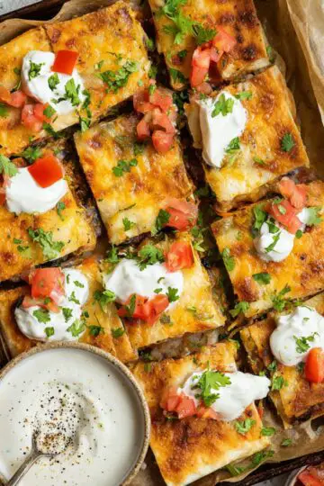 Healthy Sheet Pan Crunchwrap Recipe 4 Sheet Pan Crunchwrap A stacked plate of crispy quesadillas, topped with fresh tomato, cilantro, and a dollop of sour cream. The golden-brown quesadillas have a crispy exterior and are filled with flavorful ingredients.