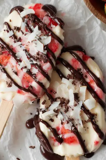 Healthy Strawberry Yogurt Clusters Recipe 1 Strawberry Yogurt Clusters Four freshly poured strawberry yogurt popsicles on wooden sticks with diced strawberries visible, placed on white parchment paper before freezing