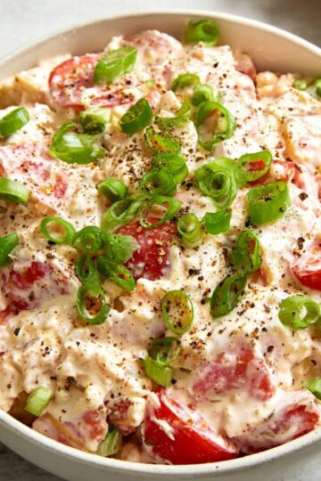 Healthy Tomato Cracker Salad Recipe 1 Tomato Cracker Salad A finished tomato cracker salad served in a white bowl, topped with sliced green onions and freshly cracked black pepper, with tomatoes and crackers visible in the creamy dressing.