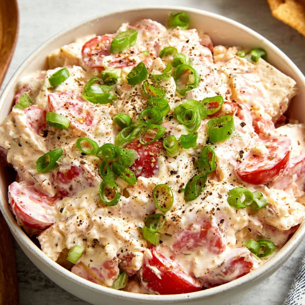 Tomato Cracker Salad A finished tomato cracker salad served in a white bowl, topped with sliced green onions and freshly cracked black pepper, with tomatoes and crackers visible in the creamy dressing.
