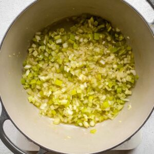 A gray pot containing sautéed diced celery and onions as the base for clam chowder, glistening in oil and beginning to soften.