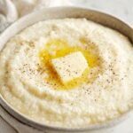 creamy grits A bowl of creamy grits served with a pat of melting butter on top, sprinkled with black pepper, highlighting a ready-to-eat breakfast presentation.