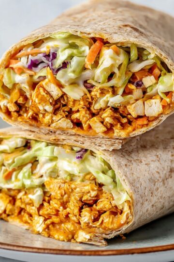 Healthy Shredded Tofu Wraps Recipe 1 shredded tofu wraps Two buffalo tofu wraps cut in half and stacked, showing shredded buffalo tofu and slaw tightly rolled inside whole wheat tortillas on a plate.