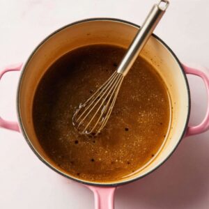 The Best Baked Peaches Recipe 15 A pink pot containing a brown mixture being stirred with a whisk.