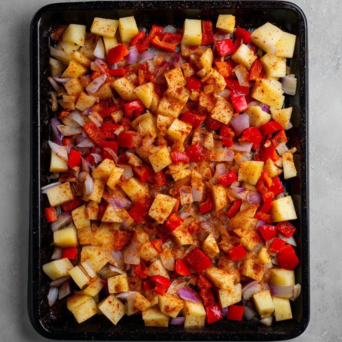 Best Black Bean Burritos Recipe 10 A tray filled with chopped potatoes, red bell peppers, and onions, all seasoned with a vibrant mix of spices like paprika, ready to be roasted in the oven for a delicious side dish.