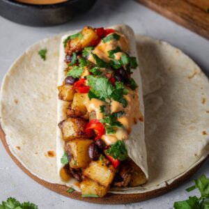 Best Black Bean Burritos Recipe 18 A tortilla wrap filled with roasted potatoes, red peppers, black beans, and a creamy, spicy sauce, topped with fresh cilantro for a fresh, flavorful bite.