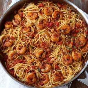 Healthy Blackened Shrimp Pasta Recipe 17 A skillet filled with spaghetti mixed with tomato sauce and topped with browned shrimp, evenly distributed throughout the pasta.