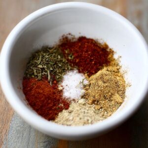 Healthy Blackened Shrimp Pasta Recipe 14 A small white bowl containing a mix of different spices, including red pepper, dried herbs, garlic powder, and salt, arranged separately inside the bowl.