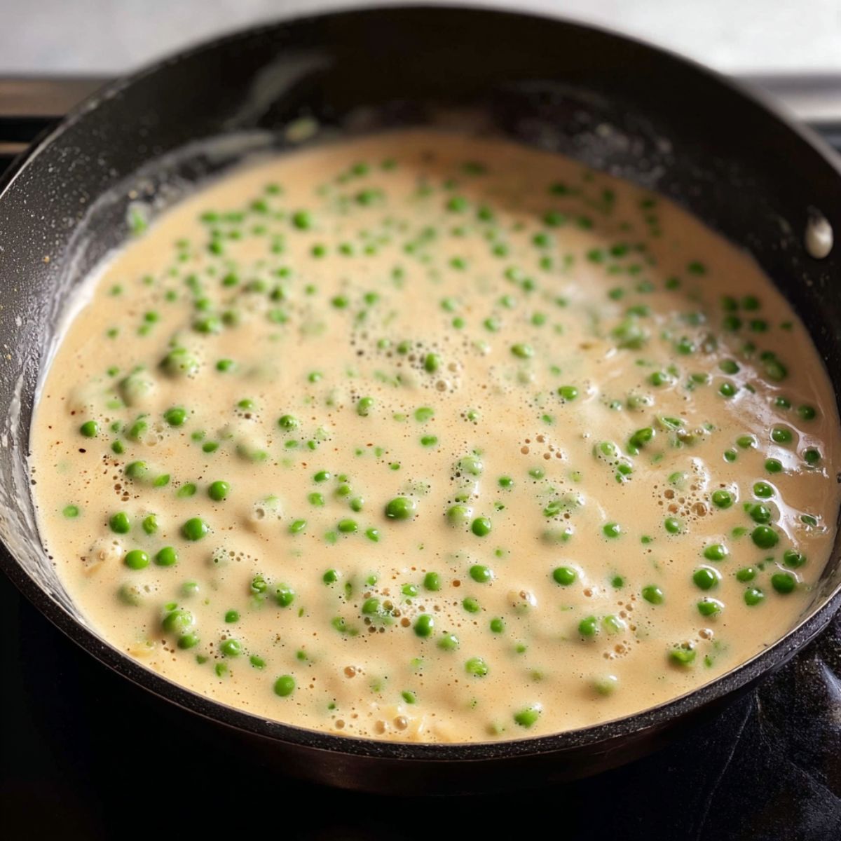 Healthy Chicken Asparagus Pasta Recipe 12 A creamy sauce with green peas simmering in a black skillet, creating a thick, smooth mixture.