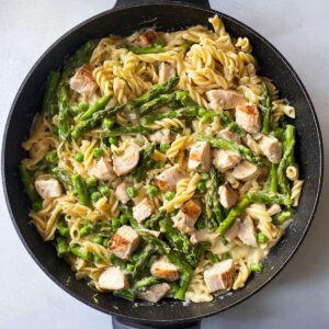 Healthy Chicken Asparagus Pasta Recipe 18 Cooked pasta, asparagus, peas, and diced chicken mixed together in a skillet with creamy sauce.