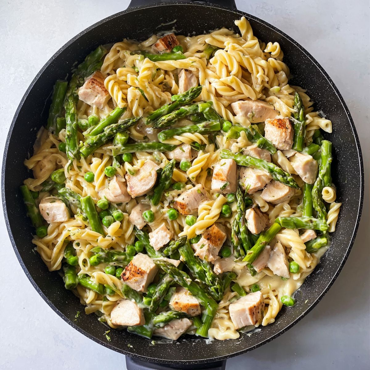 Healthy Chicken Asparagus Pasta Recipe 13 Cooked pasta, asparagus, peas, and diced chicken mixed together in a skillet with creamy sauce.