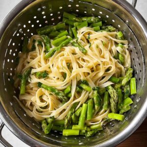 Healthy Chicken Asparagus Pasta Recipe 15 A colander filled with cooked fettuccine pasta and chopped green asparagus pieces, ready to be combined with other ingredients.