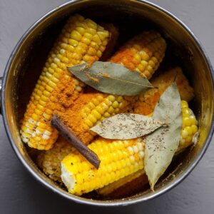 Best Chicken Broth Recipe 13 Corn cobs in a pot with added spices such as turmeric, bay leaves, and black pepper, ready for cooking