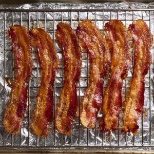 Crispy bacon strips on a wire rack over a foil-lined baking sheet, oven-baked, top-down view, golden brown texture, high detail, evenly cooked, ready to use for a sandwich.