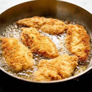 Easy Chicken Parmesan with Spaghetti Recipe 16 Breaded chicken breasts frying in a skillet with bubbling oil, forming a golden crust.