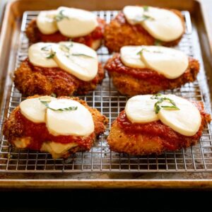 Easy Chicken Parmesan with Spaghetti Recipe 17 Fried chicken breasts placed on a wire rack over a baking sheet, topped with marinara sauce and slices of mozzarella cheese.