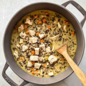 Delicious Chicken Wild Rice Soup Recipe 16 Overhead view of a grey pot filled with chicken wild rice soup, showing cubed chicken, wild rice, carrots, and creamy broth. The soup is partially stirred with a wooden spoon.