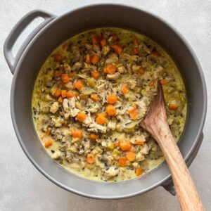 Delicious Chicken Wild Rice Soup Recipe 14 Overhead view of a grey pot filled with chicken wild rice soup in the process of cooking, showing mixed vegetables, chicken pieces, and wild rice in a creamy broth with a wooden spoon.