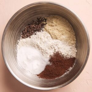 Healthy Chocolate Hot Cross Buns Recipe 15 A metal mixing bowl containing dry ingredients for chocolate dough, including flour, sugar, cocoa powder, and yeast.