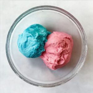 Easy Cotton Candy Cookies Recipe 15 Overhead view of two balls of cookie dough in a clear bowl. One dough ball is bright blue, and the other is pink, showing that the dough has been colored for a fun, vibrant cookie.