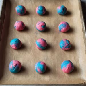 Easy Cotton Candy Cookies Recipe 16 Baking sheet lined with parchment paper holding several small balls of marbled pink and blue cookie dough, spaced evenly for baking.