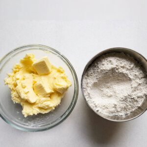 Easy Cotton Candy Cookies Recipe 14 Overhead view of two glass bowls on a white surface. One bowl contains creamed butter and sugar, and the other bowl contains flour, ready to be combined for cookie dough.