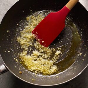 The Best Creamy Salmon Pasta Recipe 15 "Minced garlic sautéing in melted butter in a pan with a red spatula."